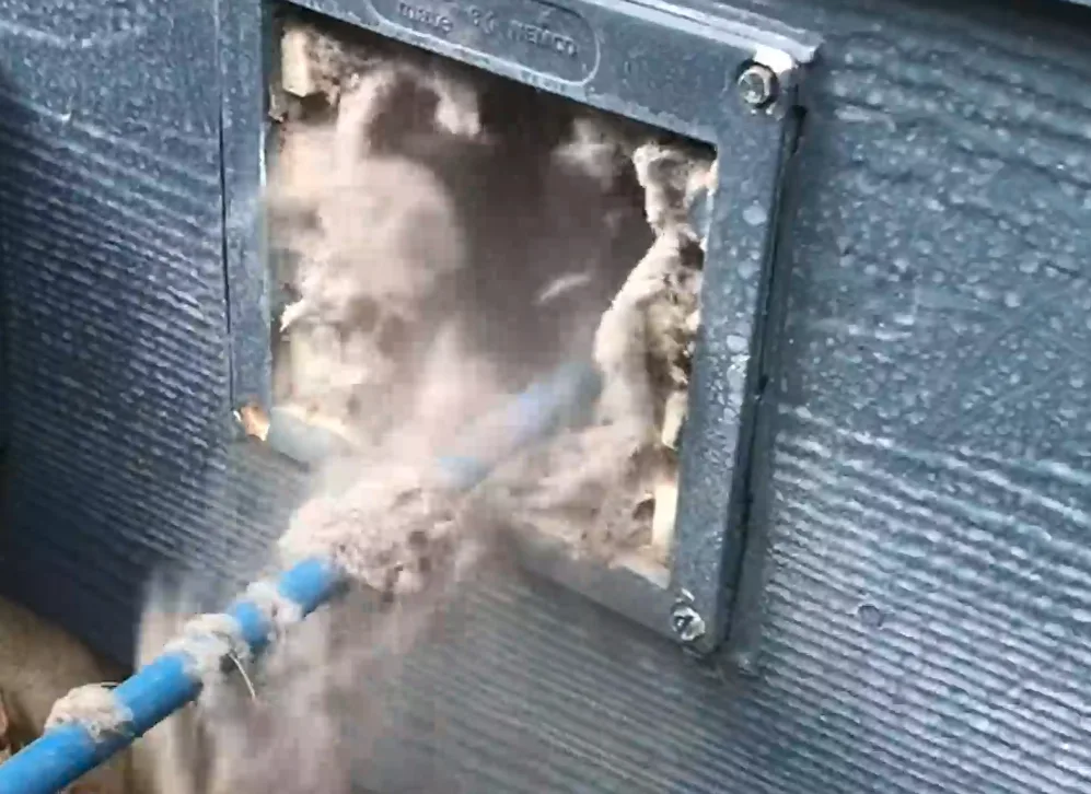 Dryer vent being cleaned with compressed-air whip, dislodging heavy lint buildup